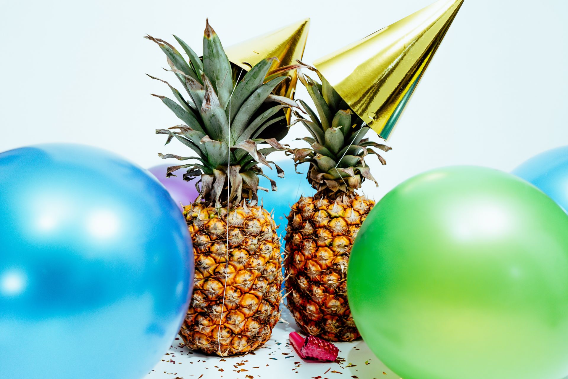 2 Ananas mit Partyhüten und Luftballons.